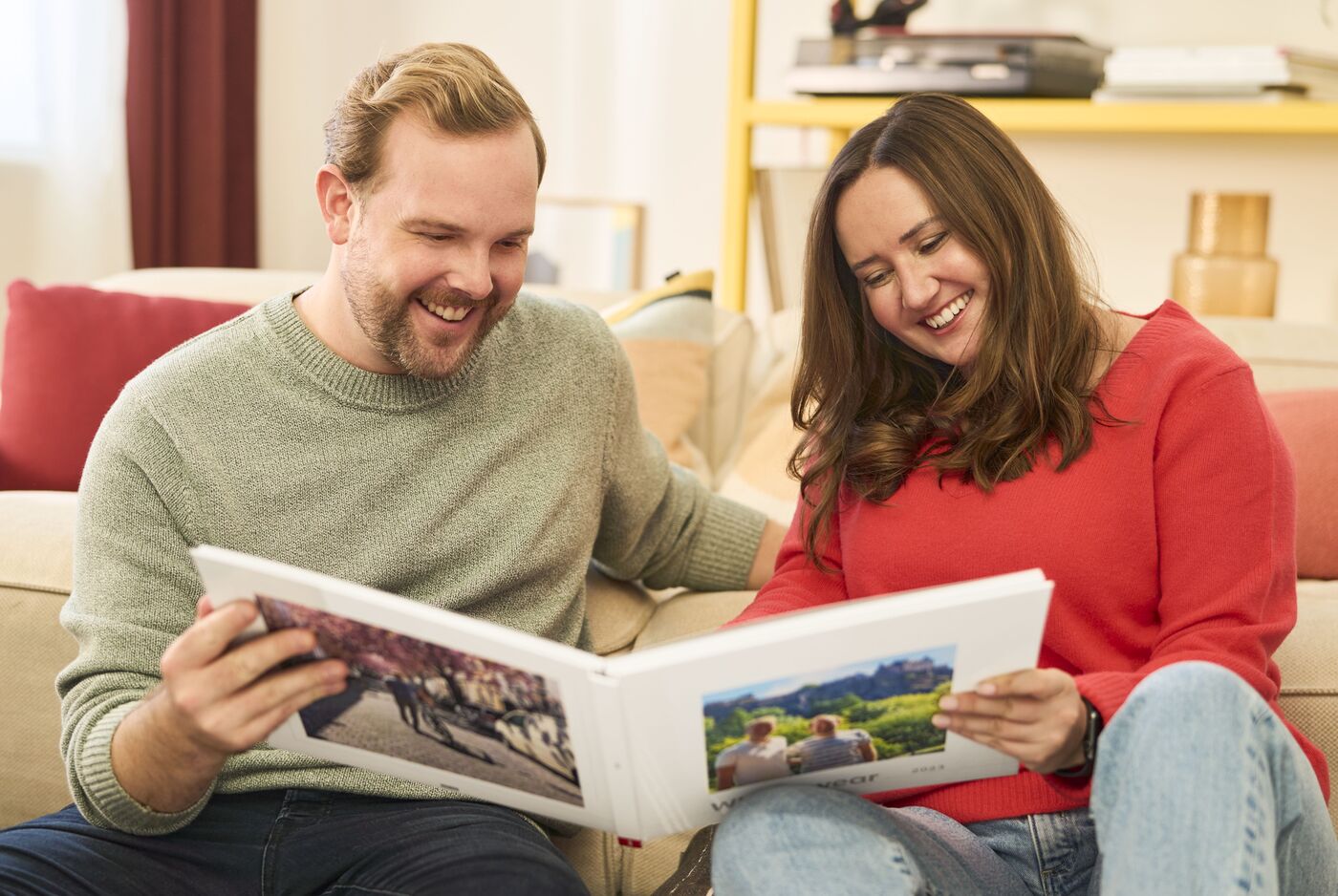 Ein Paar sitzt gemütlich auf dem Sofa und schaut aufmerksam ein Fotobuch an. Es werden schöne Erinnerungen durchblättert.