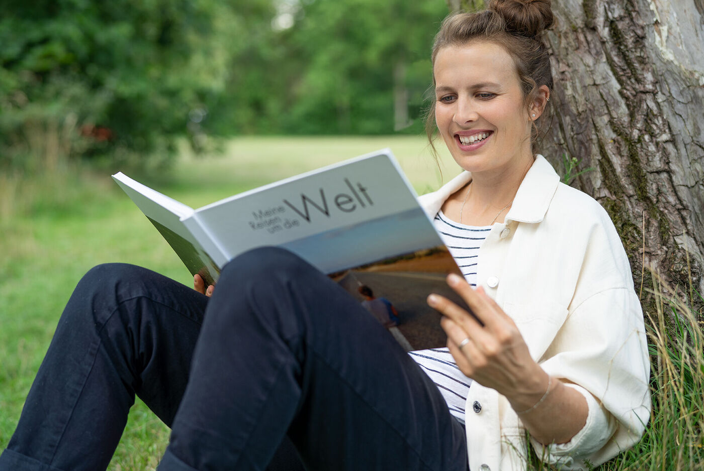 Eine Person sitzt unter einem Baum und liest ihr CEWE Fotobuch.