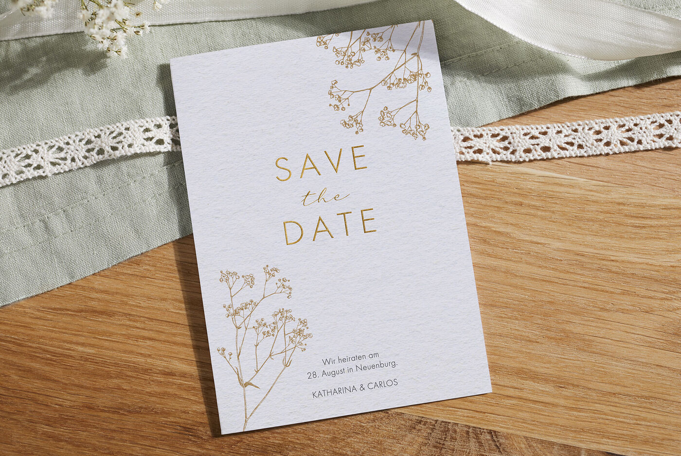 Ein elegantes "Save the Date"-Kärtchen mit floralen Elementen in Gold und einem romantischen Schriftzug