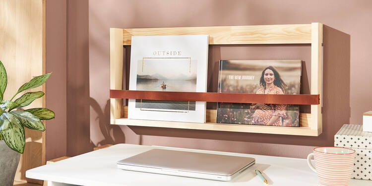 Ein Holzregal hängt an einer Wand über einem Schreibtisch. Darauf stehen zwei selbst gestaltete Fotobücher, die Cover zeigen zum Betrachter.