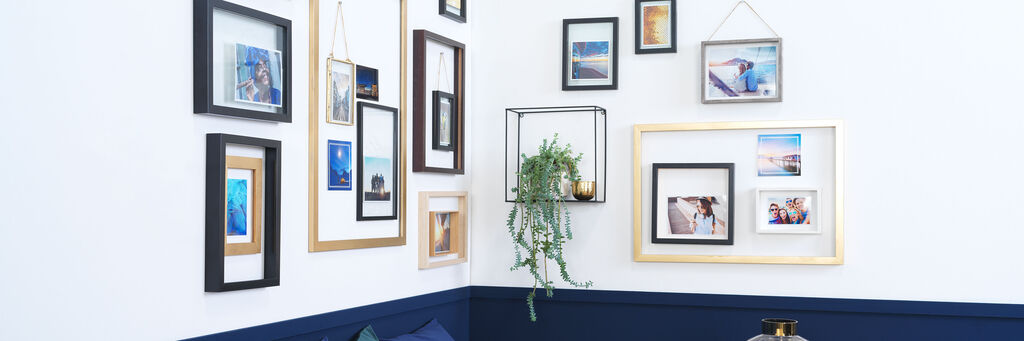 Ecksofa mit Esstisch über dem viele Bilder in diversen Rahmen und ein metallisches Regal, auf der eine Planze steht, an der Wand hängen.