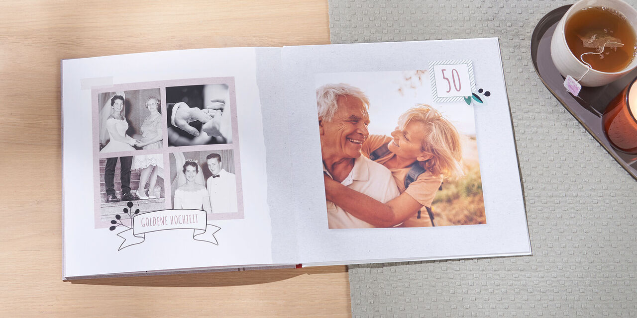 Auf einem Tisch liegt ein offenes CEWE FOTOBUCH. Links sieht man alte Schwarzweißbilder eines frisch vermählten Ehepaars auf ihrer Hochzeit vor 50 Jahren. Rechts ist ein aktuelles Bild vom Ehepaar am 50. Jahrestag zu sehen. Neben